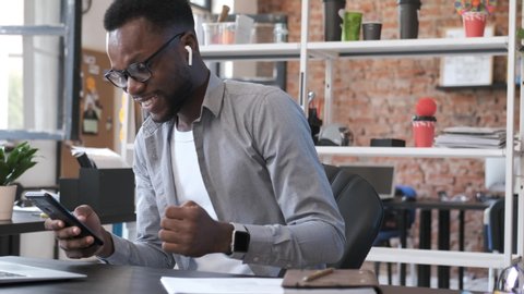 Happy African American man look at smartphone screen overjoyed by great news. Motivated businessman reading excellent online message. Good work result. Emotions of young man from business success.