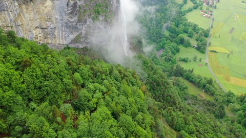 Aerial Forward: Thin Waterfall Among Lush Green on Stunning Mountain over Picturesque Town - Chamonix, France