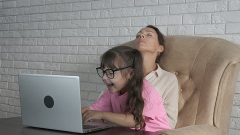 Mom at the computer. A tired woman from the computer lays on a chair, a little girl puts on glasses and insists on working on a computer.