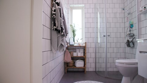 [WIDE ANGLE] Slow pan left of a modern Scandinavian bathroom with towels, bamboo shelf, toilet paper and decorations.