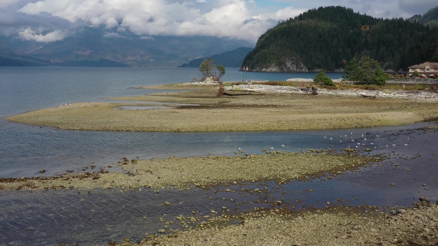 Aerial view over inlet, ocean and island with boat and mountains in beautiful British Columbia. Canada. 4K.