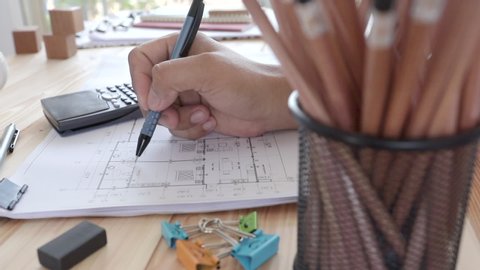 Engineers drawing home on the wood table, Architect design of house placed
on wooden table, Male hands draw with a pencil and other drawing tools, Manipulator outline residence, Closeup slider view