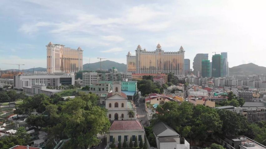 Rising drone reveal shot of Taipa skyline in Macau with park and church in foreground and casino hotel in background