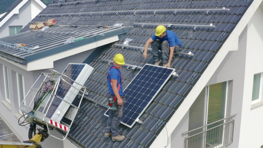 Two workers on the roof discussing, how to put the first panel in the place - wearing blue shirts and yellow helmets | Shutterstock HD Video #1038944402