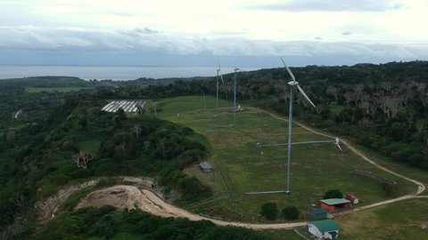 Aerial view of a wind and solar farm situated on a mountain top near the coastline of a tropical island in the Pacific ocean region