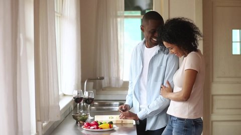 Black man stand near kitchen counter top cutting vegetables prepares salad beloved girl embraces him from behind couple inlove talking enjoy time together, romantic relations date, healthy eat concept