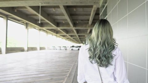 Asian Teenager girl turns around and looks at camera. Beautiful woman has long Green curl hair. Attractive fashion model is walking, shaking and flying curly green coloring hair. Slow Motion Gimbal