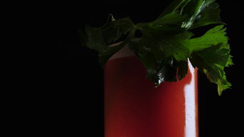 A freshly mixed Bloody Mary cocktail or healthy drink with a celery stick in a glass filled with ice isolated against black background
