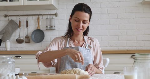 Happy young woman wear apron kneading dough for pizza with hands flour baking pastry at home, smiling lady housewife cooking in modern kitchen alone preparing pie cake or handmade cookies on table