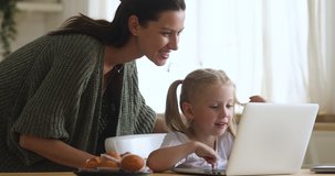 Cute kid girl learning using laptop with mom parental control sit at kitchen table, young happy mother teaching preschool little child daughter having fun online on computer notebook talking at home
