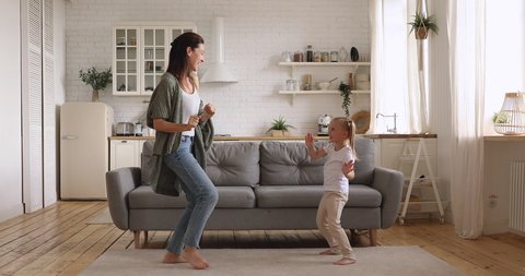 Funny cute small kid daughter copy imitate carefree young mom dancing together at home, happy family single mother and active little child girl having fun enjoy funny dance in modern kitchen interior