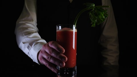 Bartender presents a freshly mixed Bloody Mary drink cocktail against a black background
