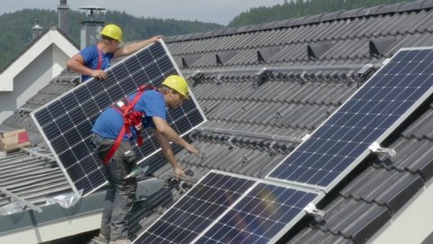 Workers installing PV (Photovoltaic) solar panels on the roof of a house,which converts solar energy into electric energy.A static footage.Concept of job,work,duty,professionalism.(2)