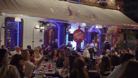 Thessaloniki, Greece - October 12 2019: Hellenic nightlife video of people at outdoors tavern restaurants. Crowd eating & drinking at illuminated taverna with live bouzouki music at Ladadika area.