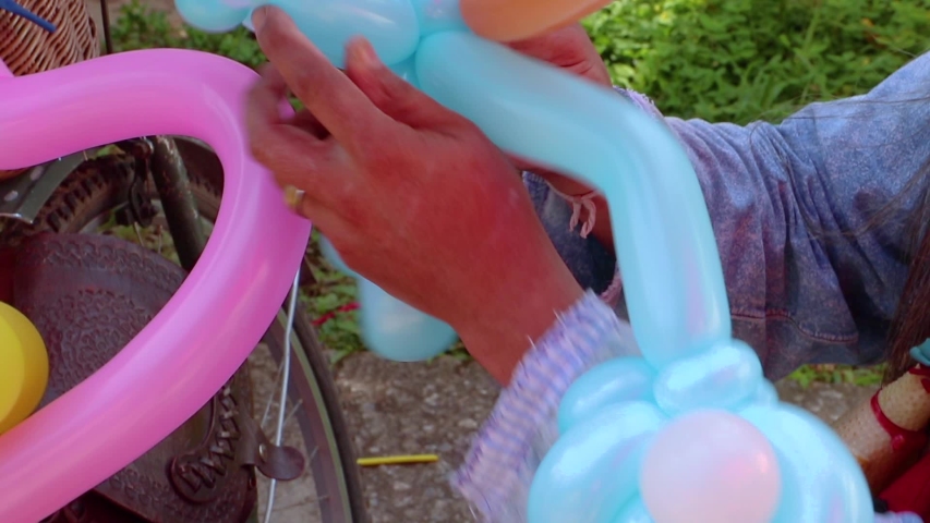 A freelance clown creating balloon animals and different shapes at outdoor festival in city centre. School bag, angel wings, butterflies and dogs made of balloons. Concept of entertainment, birthdays