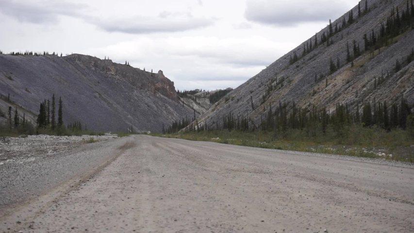 Low shot of an extreme truck camper appearing from the right of the shot on a dirt road. Dempster Highway, Canada.