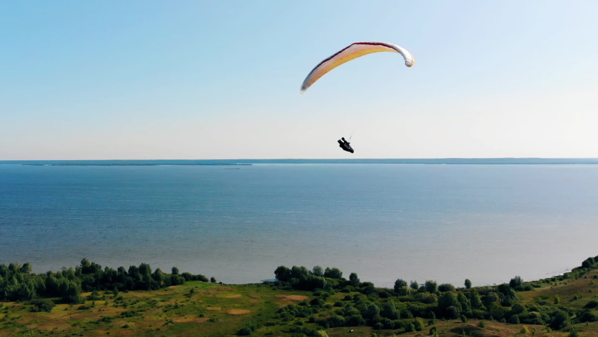 Green land and fast paragliding flight above it. Man Paragliding. beautiful nature background.