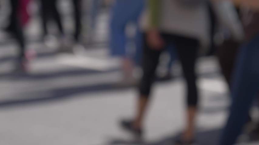 Blurred crowd of people feet marching on a street on a sunny day.