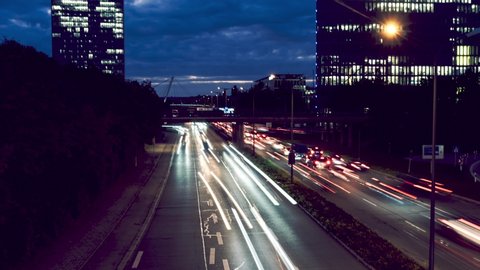 Timelapse of car traffic jam at busy street road highway long exposure light trails during dark evening night with munich skyline background