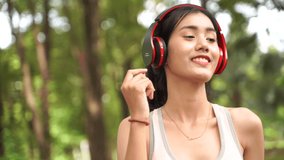 Slow motion video Healthy woman are listening to music during exercise in a happy relaxing mood at the park with green leaves blur bokeh background and sunlight in sport and healthy concept