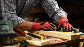 Adult carpenter craftsman wears protective gloves, with a pencil and the carpenter's square trace the cutting line on a wooden table. Construction industry, housework do it yourself. Footage.