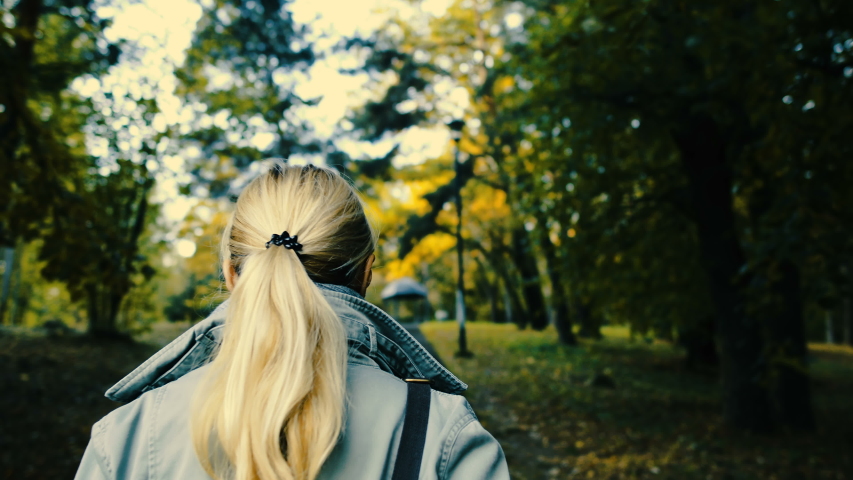 Walk in the autumn park. Girl walks through the autumn city park on a sunny warm day. Yellow and orange leaves are on the ground. Golden autumn.