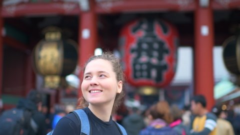 Asakusa area in Tokyo, Japan with young caucasian girl woman by Sensoji temple shrine gate entrance with red architecture panning up in slow motion