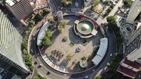 Aerial top view of a roundabout in Mexico City with lots of traffic and people walking in a public plaza during sunset.