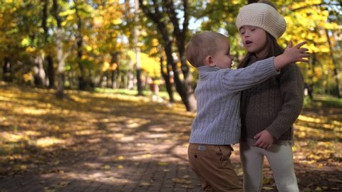 Close-up of joyful toddler siblings cuddling in autumn park, little boy hugging and kissing his older sister with down syndrome. Happy children expressing mutual love while spending freetime outdoors