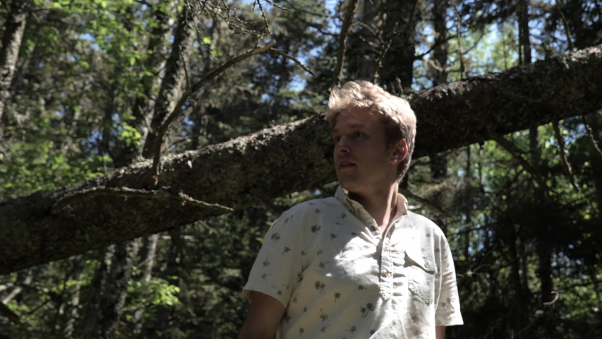 Caucasian male with blonde hair walks forward through a lush green jungle