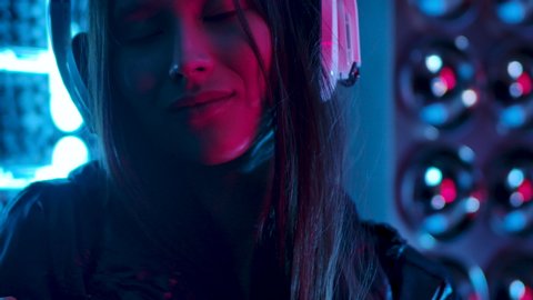 Portrait of Elegant 30s Girl Who Listening to Music in Earphones and Dancing on Party Enjoy Evening in Slow Motion. Young Beautiful Woman Looking at Camera Indoors with Colorful UV Light Close up 4K 