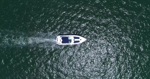 Top view, rising drone shot, of a white and blue yacht, on a bright and clean ocean with nothing around, leaving a water trail behind it, on a sunny day