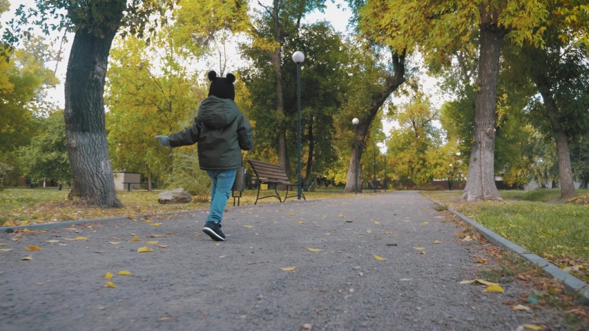 Happy baby boy running in autumnal park. Little child playing on autumn walk. Autumnal forest with golden leaves. Steadicam video, 4K slow motion.