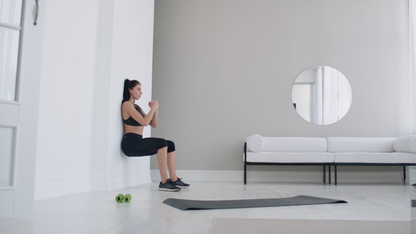 A woman in a static position carries out a grueling exercise leaning against a wall in a sitting position. Endurance training