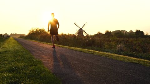 Man running in the Dutch countryside near a traditional windmill. Groningen, Holland.