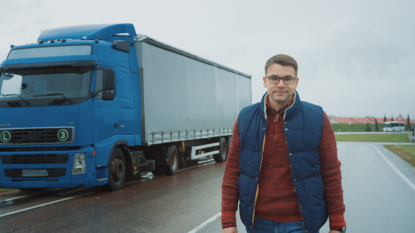 Professional Young Truck Driver Crosses Arms and Smiles. Behind Him Parked Blue Long Haul Semi-Truck with Cargo Trailer Royalty-Free Stock Footage #1039037192