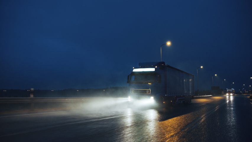 Blue Long Haul Semi-Truck with Cargo Trailer Full of Goods Travels At Night on the Freeway Road, Driving Across Continent Through Rain, Fog, Snow. Industrial Warehouses Area. Front Following Shot | Shutterstock HD Video #1039037246