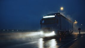Blue Long Haul Semi-Truck with Cargo Trailer Full of Goods Travels At Night on the Freeway Road, Driving Across Continent Through Rain, Fog, Snow. Industrial Warehouses Area. Front Following Shot - Powered by Shutterstock - Get 15% off with code: PIKWIZARD15
