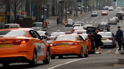 SEOUL, SOUTH KOREA - MARCH 29, 2018: Unidentified woman catch orange taxi at street of Seoul city, telephoto perspective. Wide road at Yeoksam area of Gangnam district, several taxi cars ready next