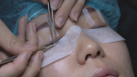 Eyelash extension and gluing artificial eyelashes with tweezers for Asian woman eye.