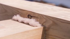 Close up of two crossed wooden beams for building a house under the bright sun. Clip. Part of wooden building construction with white thermal insulation.