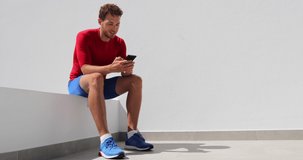 Athlete man texting looking at phone screen at home after working out training. Technology and sports athlete holding mobile phone. Happy fit young adult in compression clothing sportswear.