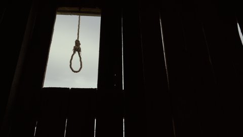 Loop neck of suicide from old rope hanging wooden background. Dark cloudy day loop horror sway from wind close up on square for gallow hangman 4K. Scary gallows time Inquisition stand on Halloween.
