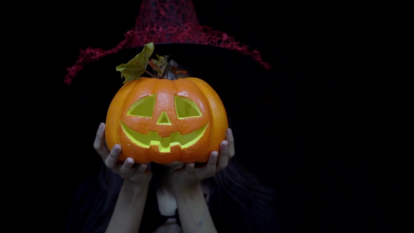 Playful woman in Halloween costume hiding and showing funny face behind Halloween pumpkin or Jack O Lantern