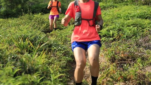 Two women trail runners running downhill on mountain slope at tropical rainforest, slow motion
