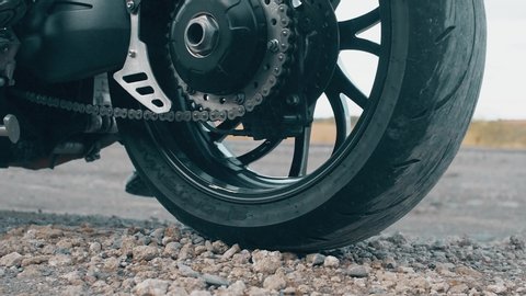 The pebbles bounce off the ground due to the rapid slippage of the motorcycle wheel. Close up slow motion footage. 4k.