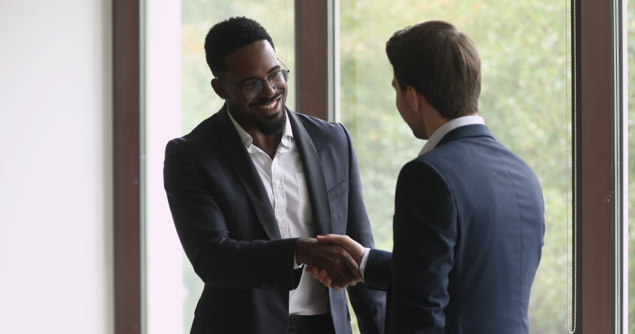 Two happy diverse businessmen talking laughing handshaking standing in office, smiling african and caucasian men executives shake hands at meeting as business agreement, corporate partnership concept Royalty-Free Stock Footage #1039082234