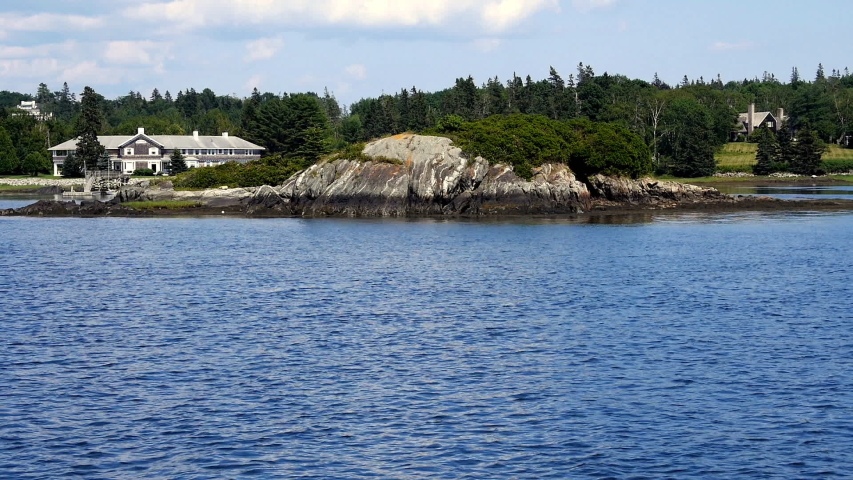 Cruising past a rocky island off the coast from a beautiful shore house in Maine