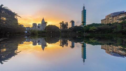 Beautiful Time lapse sunrise view of Taipei cityscape at dawn with reflection of Taipei 101 skyline by a lake in a public city park at dawn in Taiwan. Pan up motion timelapse. 4K.