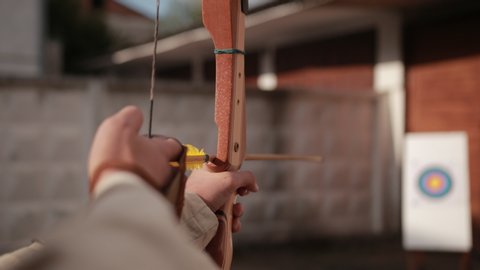 archery. guy shoots from string, wooden arrows with yellow end of fly in white foam on which hangs target, on backdrop of wall, close-up, slow motionの動画素材